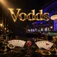 Luxurious dark casino floor with gold chips, playing cards, and ruby dice under cinematic golden and blue lighting with Vodds